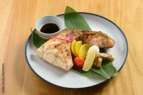 japanese cuisine hamachi kama with lemon, tomato, ginger and sauce in a plate isolated on wooden table top view photo