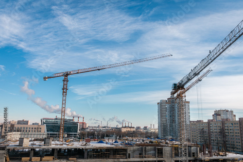 Construction cranes at a construction site in the city against the blue sky in winter conditions. Construction of a new building. The concept of building a new area.
