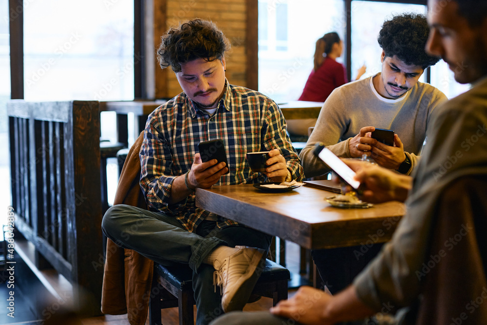 Multiracial group of young men using their smart phones while sitting in pub. Multiracial group of young men using their smart phones while sitting in pub.