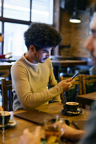 Muslim man text messaging on mobile phone while being with his friends in pub.