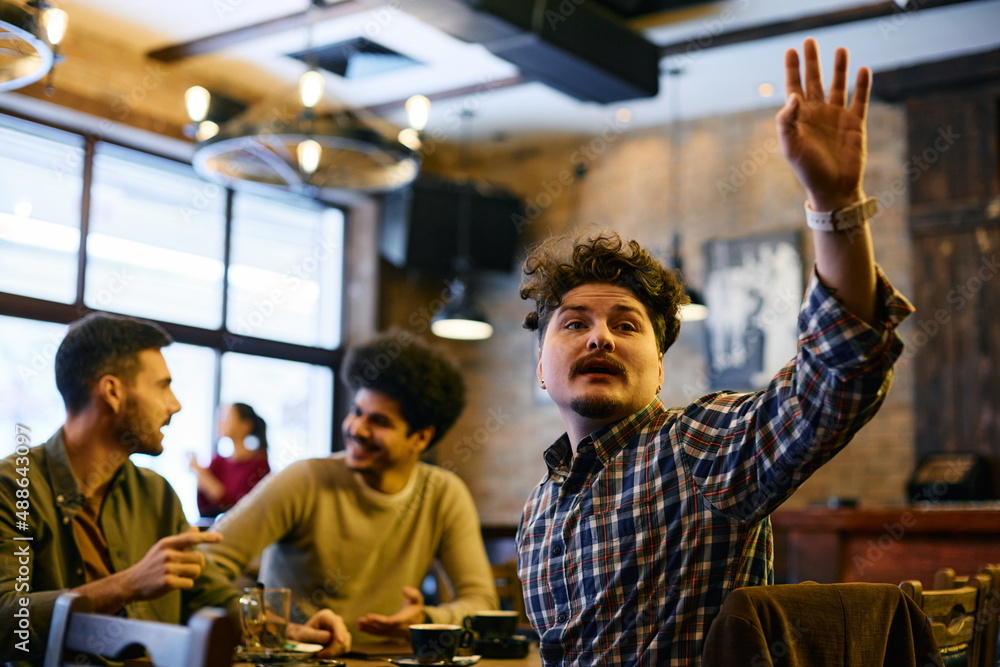 Young man raising his hand to call a waiter while being with his friends in a cafe.