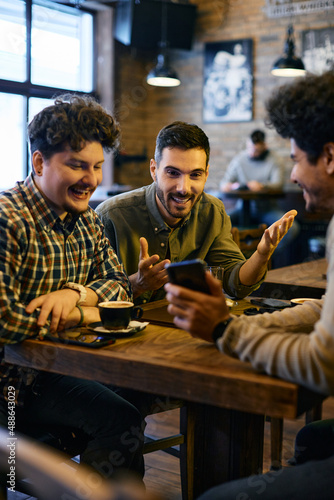 Young happy men watch sports results on smart phone while sitting in cafe.