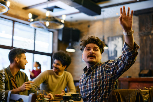 Young man raising his hand to call a waiter while being with his friends in a cafe.