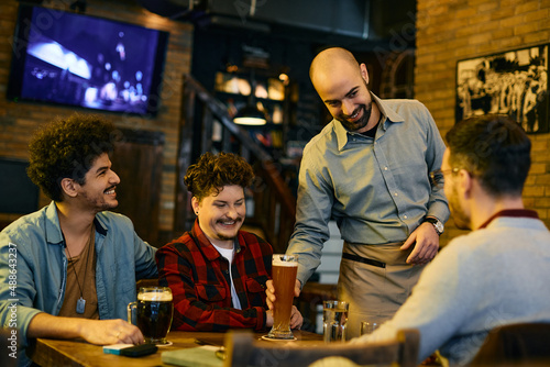 Happy waiter serving beer to group of male friends in a bar.