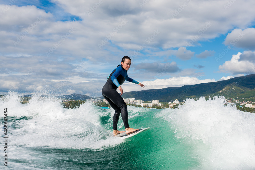 Young athletic female in wetsuit riding on endless waves behind a boat on sunny day. Woman practice wakeboarding, carving behind the baot. Watersport concept. Young athletic female in wetsuit riding on endless waves behind a boat on sunny day. Woman practice wakeboarding, carving behind the baot. Watersport concept.