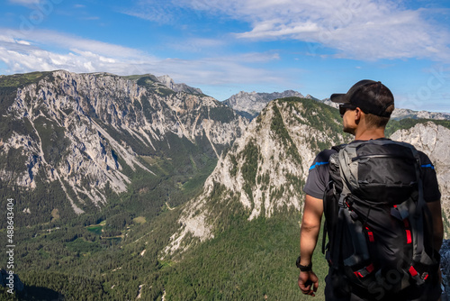 Man with a cap and a hiking backpack admiring a panoramic view on the alpine mountain chains in Austria, Hochschwab region in Styria. Freedom and adventure vibes. Oberort, Tragoess. Sunny summer day