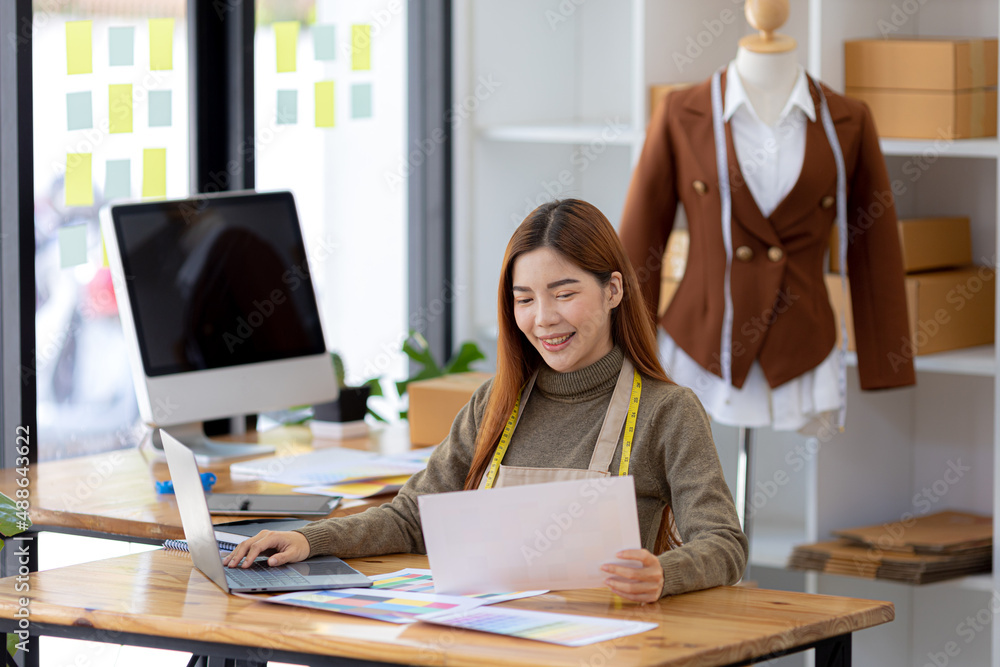 A beautiful Asian woman who owns a clothing brand, she is checking the printed designs, she designs all the clothes in her own brand and sells them online and has a storefront. Clothing design ideas.