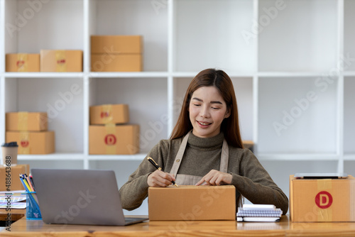 Woman who runs an e-commerce business is writing a list of customers on paper before shipping to them, she runs an e-commerce business on websites and social media. Concept of selling products online. © kamiphotos