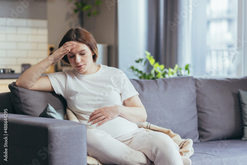 Young beautiful pregnant woman sitting at home on the couch sick, has a headache and nausea photo