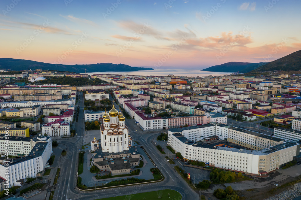 Aerial view of the city of Magadan. Beautiful morning cityscape. Top view of the Cathedral, streets and buildings. In the distance, mountains and a sea Bay. Magadan, Magadan Region, Russian Far East.