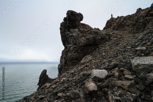Harsh arctic landscape. Rocky coast of the Arctic Ocean. On top of the rocks is a small figure of a man looking into the distance. Cape Matyushkin, East Siberian Sea, Chukotka, Far North of Russia.