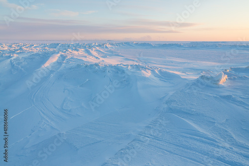 Winter arctic landscape. Cold frosty winter weather. Harsh polar climate. Ice hummocks on the frozen sea in the Arctic. View of snow and ice at sunset. Sastrugi. Wind sculpted patterns on snow surface