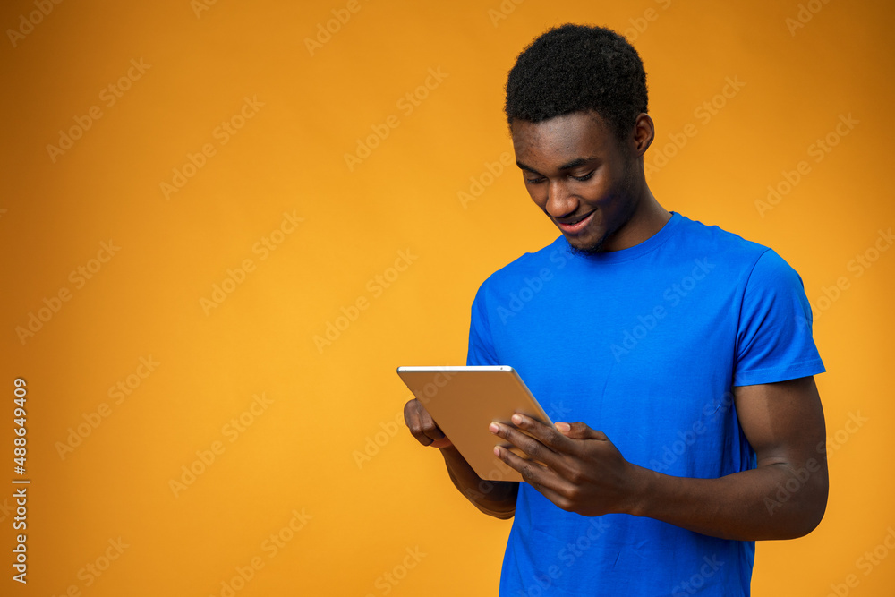 Smiling african guy using digital tablet over yellow background Smiling african guy using digital tablet over yellow background