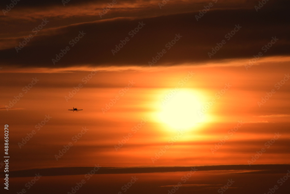 Photo of a sunset, depicting a huge sun and a small plane, against the background of the evening sky