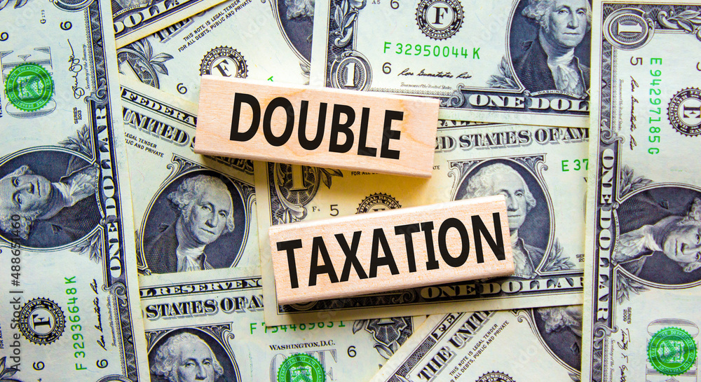 Double taxation symbol. Concept words Double taxation on wooden blocks on a beautiful background from dollar bills. Business tax and double taxation concept, copy space.