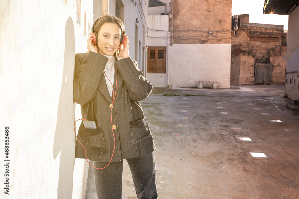 Smiling young girl in trendy jacket using earphones