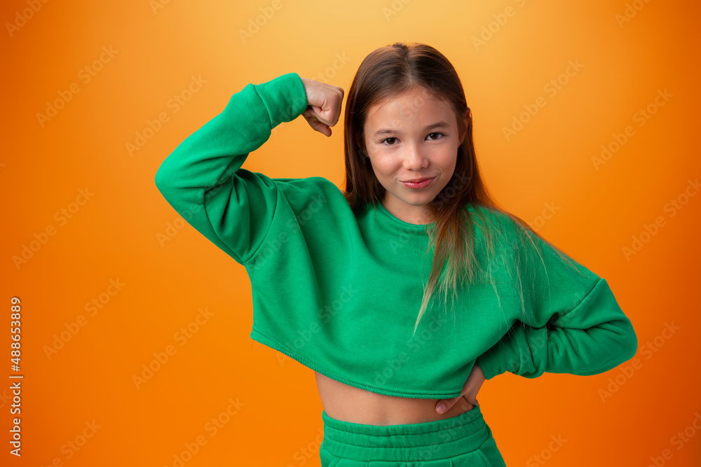 Teen girl showing off muscles biceps against orange background Teen girl showing off muscles biceps against orange background
