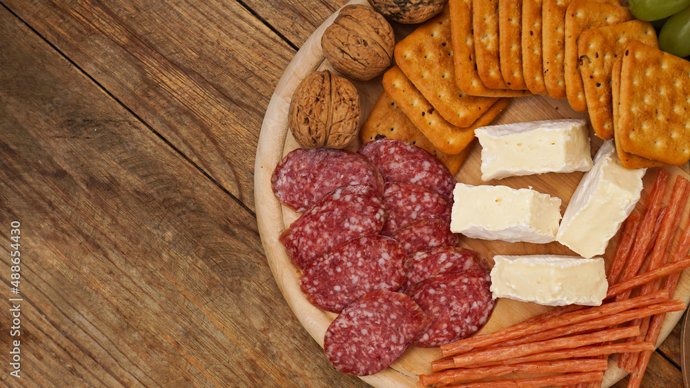 Meat and cheese plate for appetizers. Sausages, cheeses, crackers, nuts on a wooden plate and background. Top view, place for text.