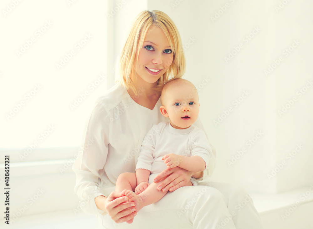 Happy smiling young mom playing with her little baby together in white room at home Happy smiling young mom playing with her little baby together in white room at home