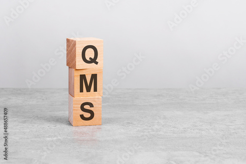 wooden cube on a table with text QMS. copy space on right for design, gray background photo