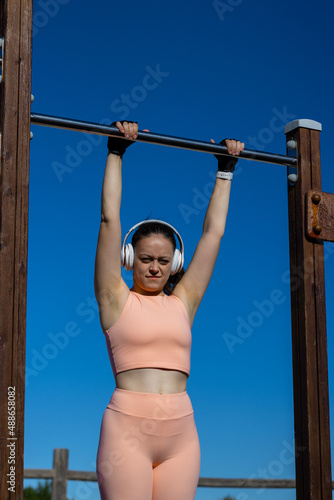 vertical portrait of a female athlete doing barbell exercise in a natural calisthenics gym outdoors