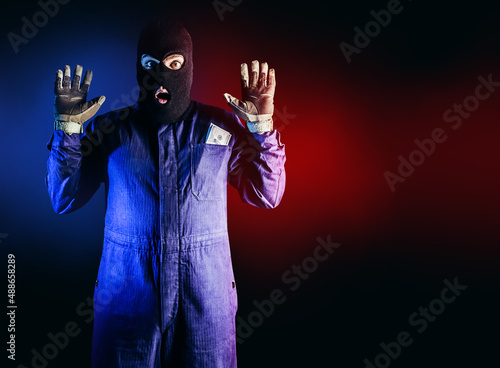 Obraz na plátně Photo of caught robber in mask, overalls, gloves and money pack standing on red and blue background