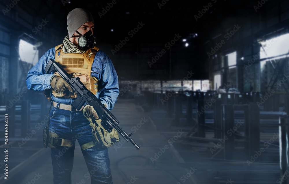 Photo of urban soldier in tactical military outfit and gas mask standing  with rifle and gas mask on dark factory background. Photos