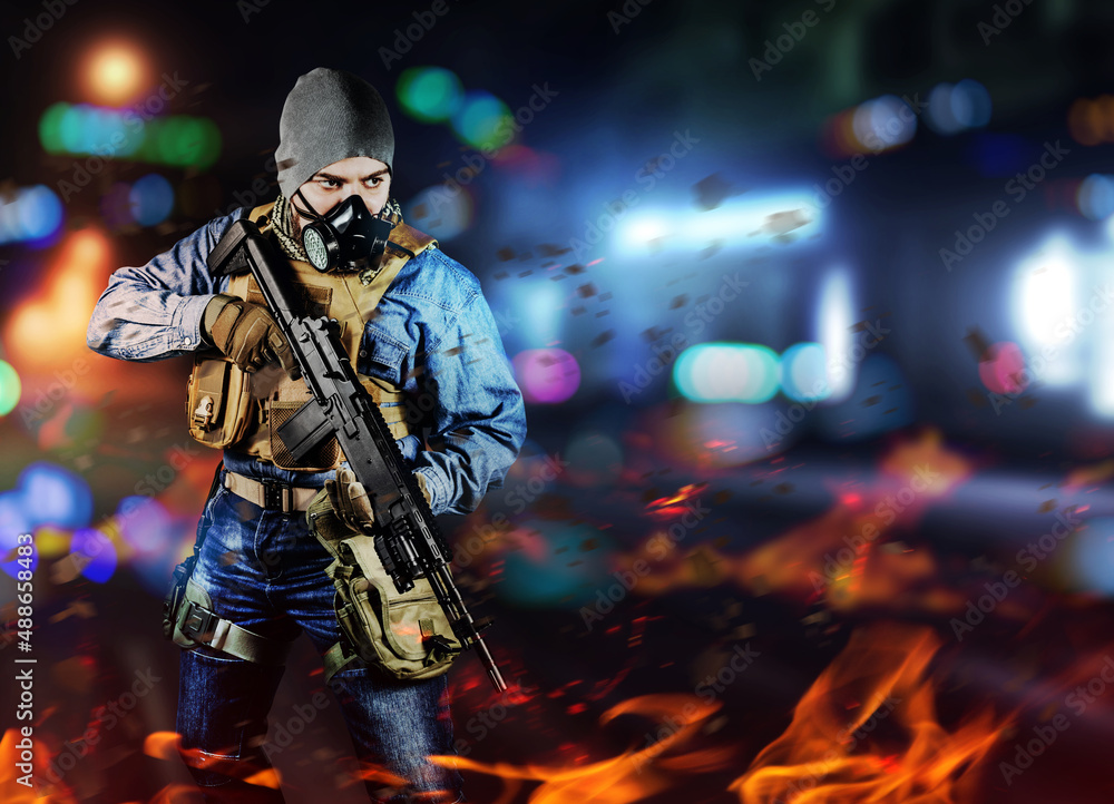Photo of urban soldier in tactical military outfit and gas mask standing with rifle and gas mask on night neon city and burning background.