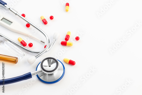 Stethoscope, glass ampoule filled with medicines and colorful pills on white background. Medical supplies and tools. Copy space for a text
