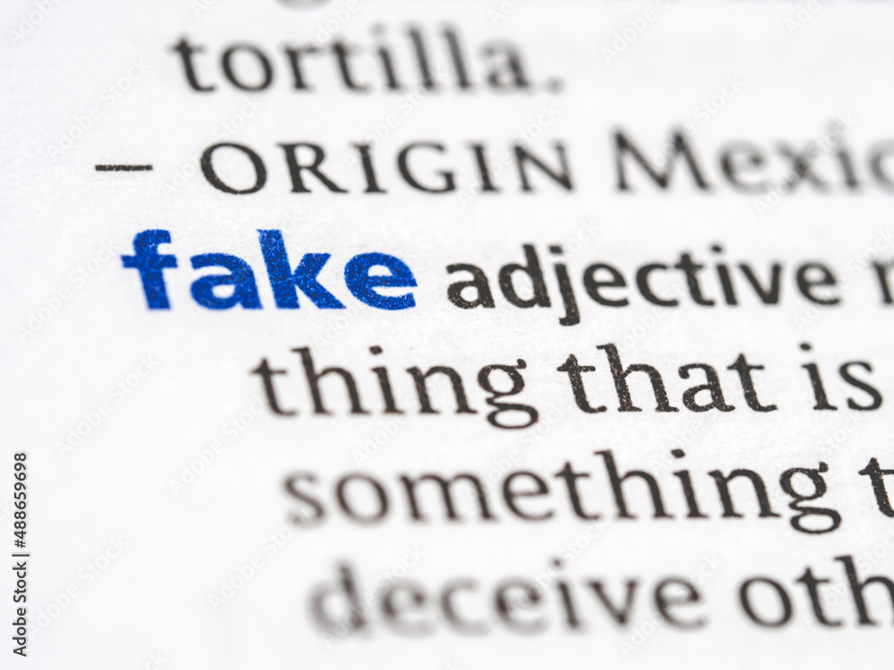 Fototapeta premium Fake - English dictionary definition of the word - photo of a dictionary page with paper grain texture - selective focus on the word