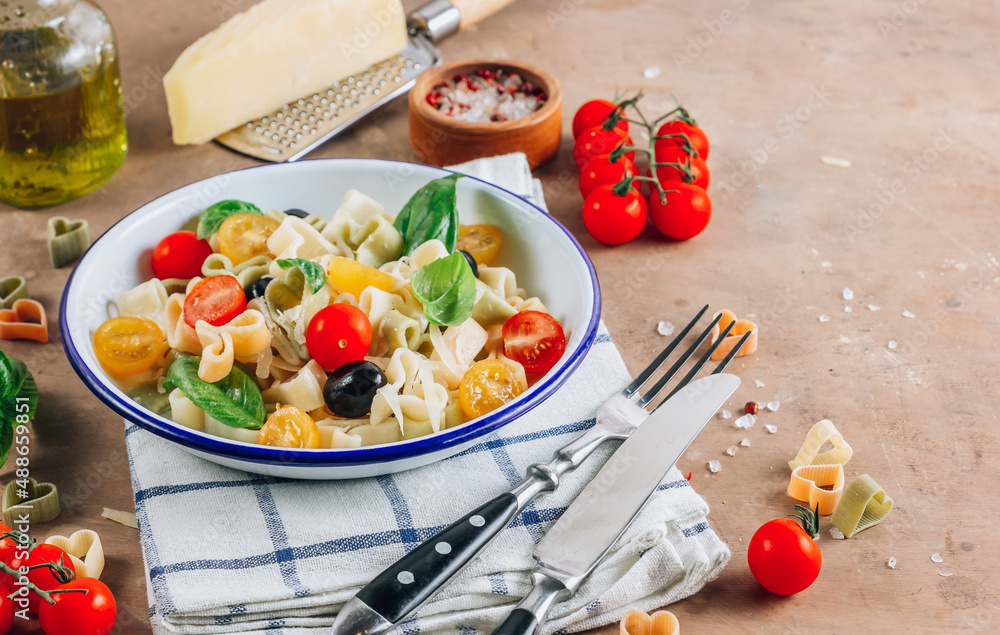 Heart pasta salad with colorful tomatoes, olives, parmesan and basil leaves
