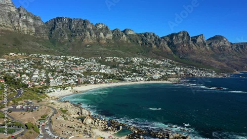 Wide aerial shot flying leftward over the ocean looking towards Camps Bay with the twelve apostle mountain range in the background photo