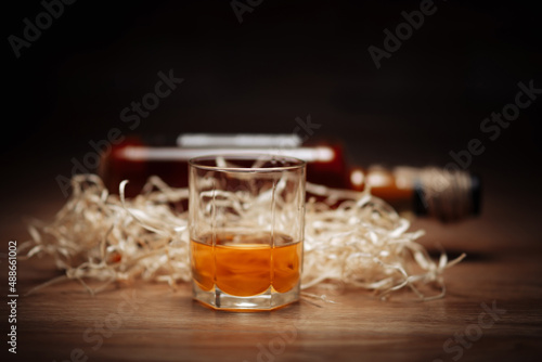 Glass of whiskey on wooden dark background with bottle