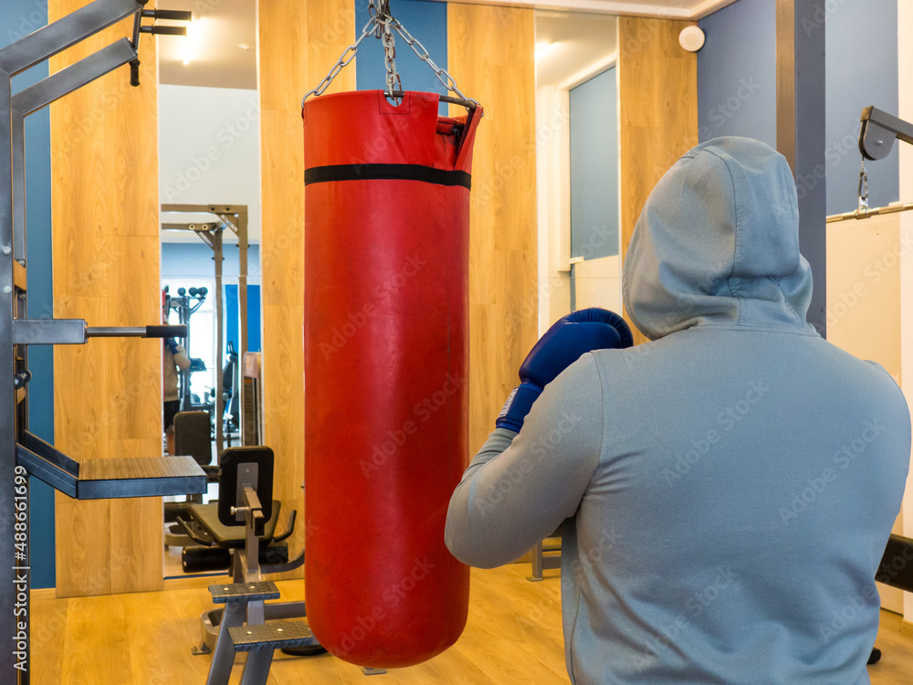 Boxing training - a hand and a red punching bag.a guy in a hood hits a punching bag