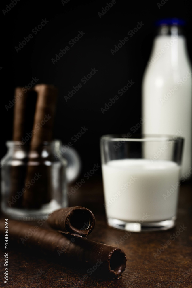 Wafer rolls in a jar on the kitchen counter. Crispy chocolate cream waffles with a glass of milk. A bottle of milk in the background. Wafer rolls in a jar on the kitchen counter. Crispy chocolate cream waffles with a glass of milk. A bottle of milk in the background.