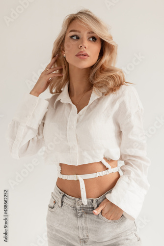 Studio portrait of a beautiful young blond woman with curly hair in a fashionable white shirt and high waisted jeans in the studio on a white background photo