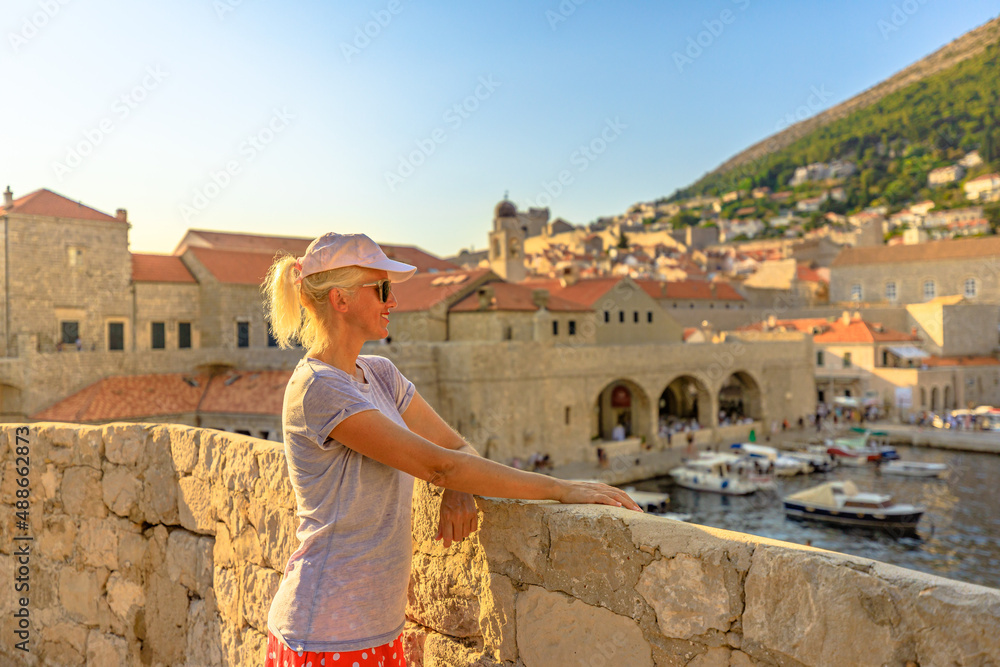 Woman looking old medieval harbour on top walls of Dubrovnik city in Croatia. Dubrovnik historic city of Croatia in Dalmatia. UNESCO Venetian architecture. Fort Lovrijenac fortress on background.