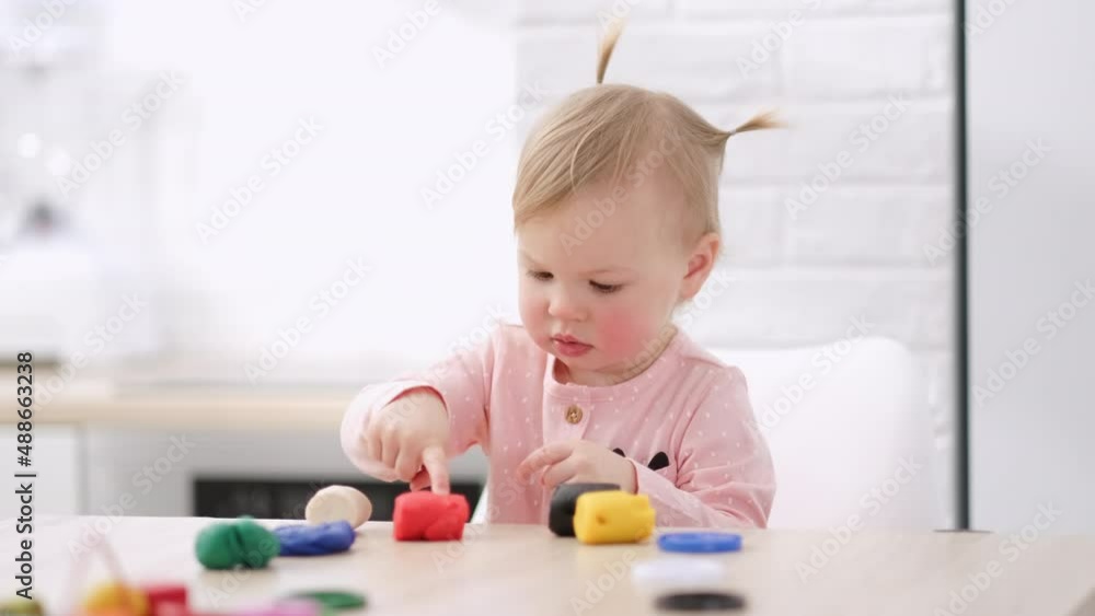 Cute Little girl with funny ponytails on head sitting in kitchen and playing multicolored plasticine, 2 years Kid girl having fun with modeling clay at home, Early education and development Cute Little girl with funny ponytails on head sitting in kitchen and playing multicolored plasticine, 2 years Kid girl having fun with modeling clay at home, Early education and development