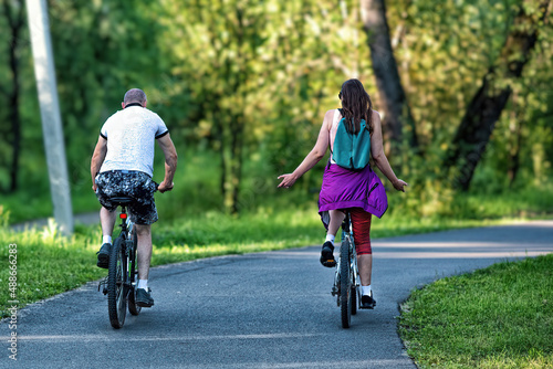 A man and a woman riding their bicycles in a park in summer in the sunny morning.