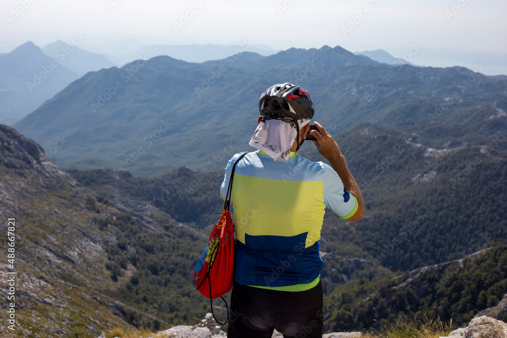Man in cycling clothes and helmet takes photo of mountain landscape on his phone
