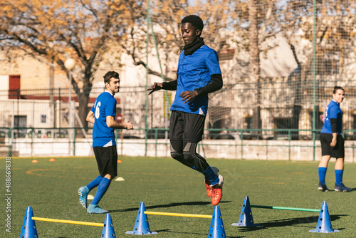 young black player jumps over hurdles at a football training session