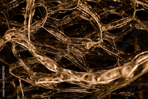 Close up photo of orange toned frozen metal fence covered in ice on dark background. photo