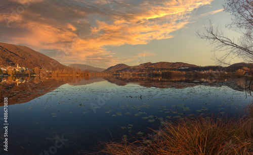Vllage of Santa Maria overlooking the lake in the middle of hills during an autumn sunset. Revine Lakes, Veneto, Italy. Concept about reflection and relaxation
