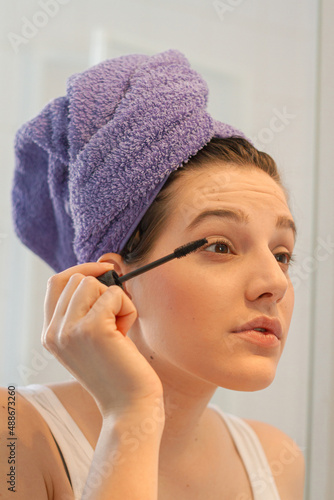 Young Woman with a towel on her head after bath applying mascara , close up
