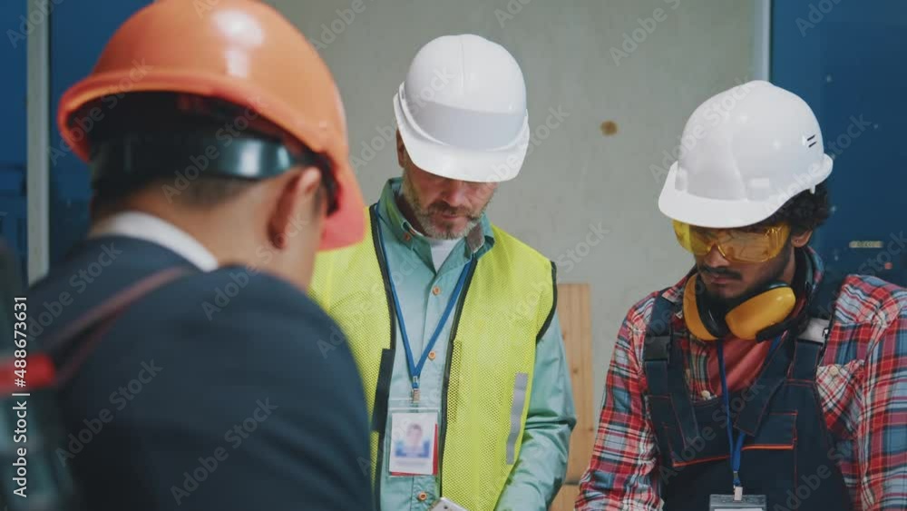 Frame below of asian architect with builders engineers in hardhats and uniforms checking blueprint and talking about construction project at construction site. Discussing building plan. Slow motion Frame below of asian architect with builders engineers in hardhats and uniforms checking blueprint and talking about construction project at construction site. Discussing building plan. Slow motion