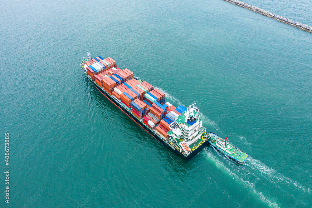 Aerial top view of cargo ship carrying container for import export goods send to customer from cargo yard port and running with tug boat  ,concept logistic and supply chain