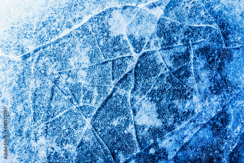 Photo of blue toned frozen cracked ice with snow surface texture.
