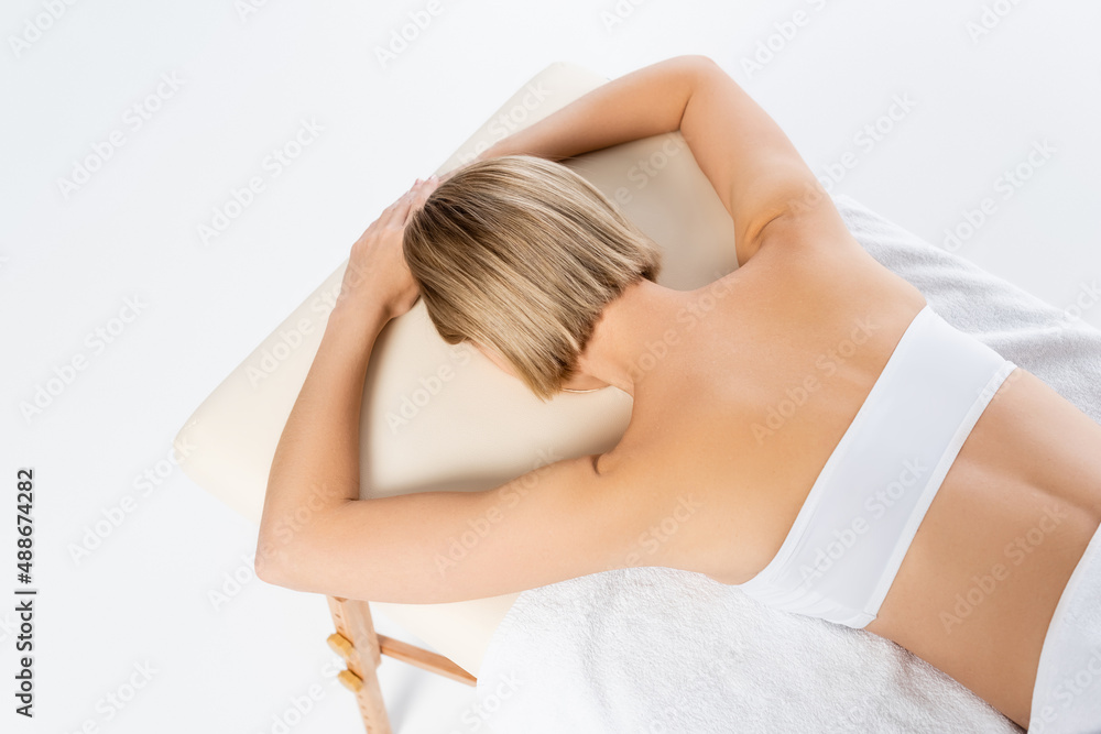 Fototapeta premium top view of blonde woman lying on massage table isolated on white
