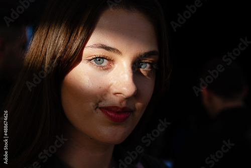 Portrait shot of beautiful young woman with blue eyes, lighten by sun ray looking at the camera