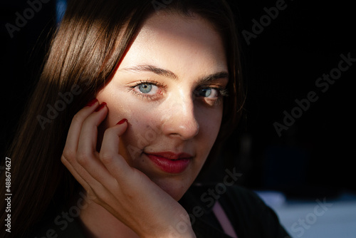 Portrait shot of beautiful young woman with blue eyes, lighten by sun ray looking at the camera
